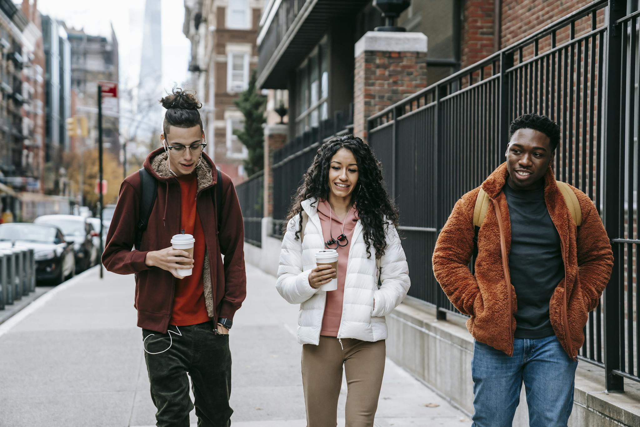 Young glad multiracial partners with hot drinks to go strolling on urban pavement in daytime
